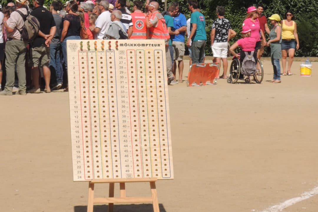 Un grand tableau de score en bois à chevilles, posé sur un chevalet lors d'un tournoi de Mölkky, avec des colonnes de trous numérotés de 0 à 50 pour quatre équipes.