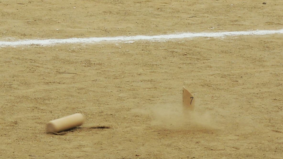 Une quille numérotée bascule dans un nuage de poussière sur un terrain de sable, le mölkky lancé déjà posé au sol à côté d'elle.